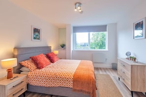Ein modernes Schlafzimmer mit Bett, Nachttischen, einer Kommode, einem Fenster mit Blick und einer Deckenleuchte.