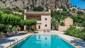A swimming pool with a stone deck, a lounge area with chairs, and a building with a tiled roof. - Kamares Private Pool Stone Villa (Apokoronas)