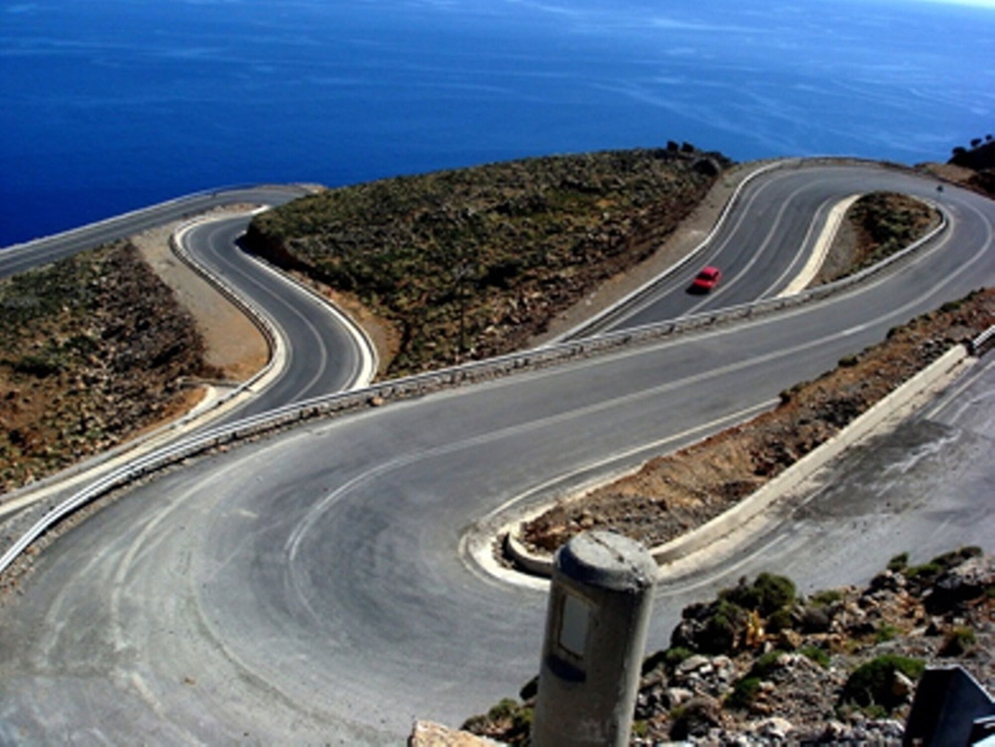 A winding road with a red car on a coastal landscape.