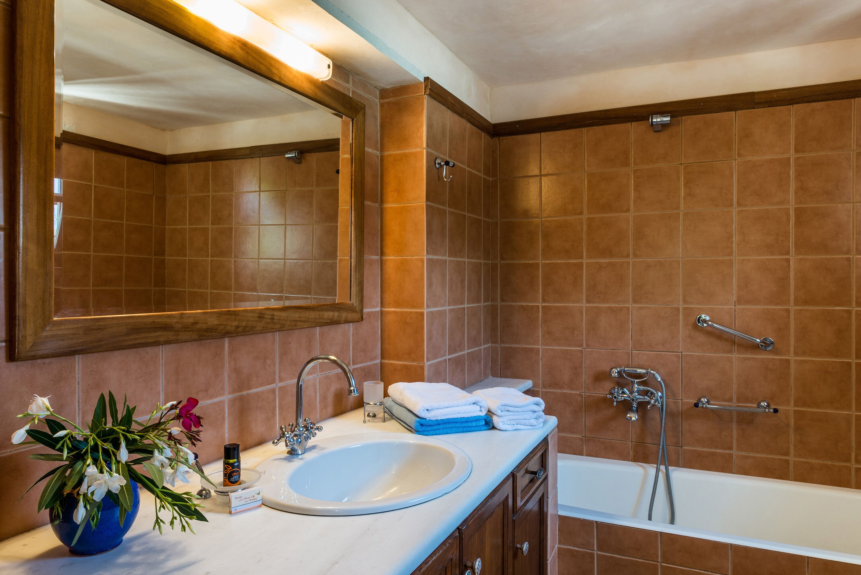 Un baño con un lavabo blanco, un espejo, una ducha y un jarrón azul con flores.