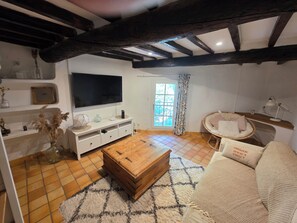 Ein Wohnzimmer mit Fernseher, Couch, Holz-Couchtisch und einem Fenster mit Vorhängen.