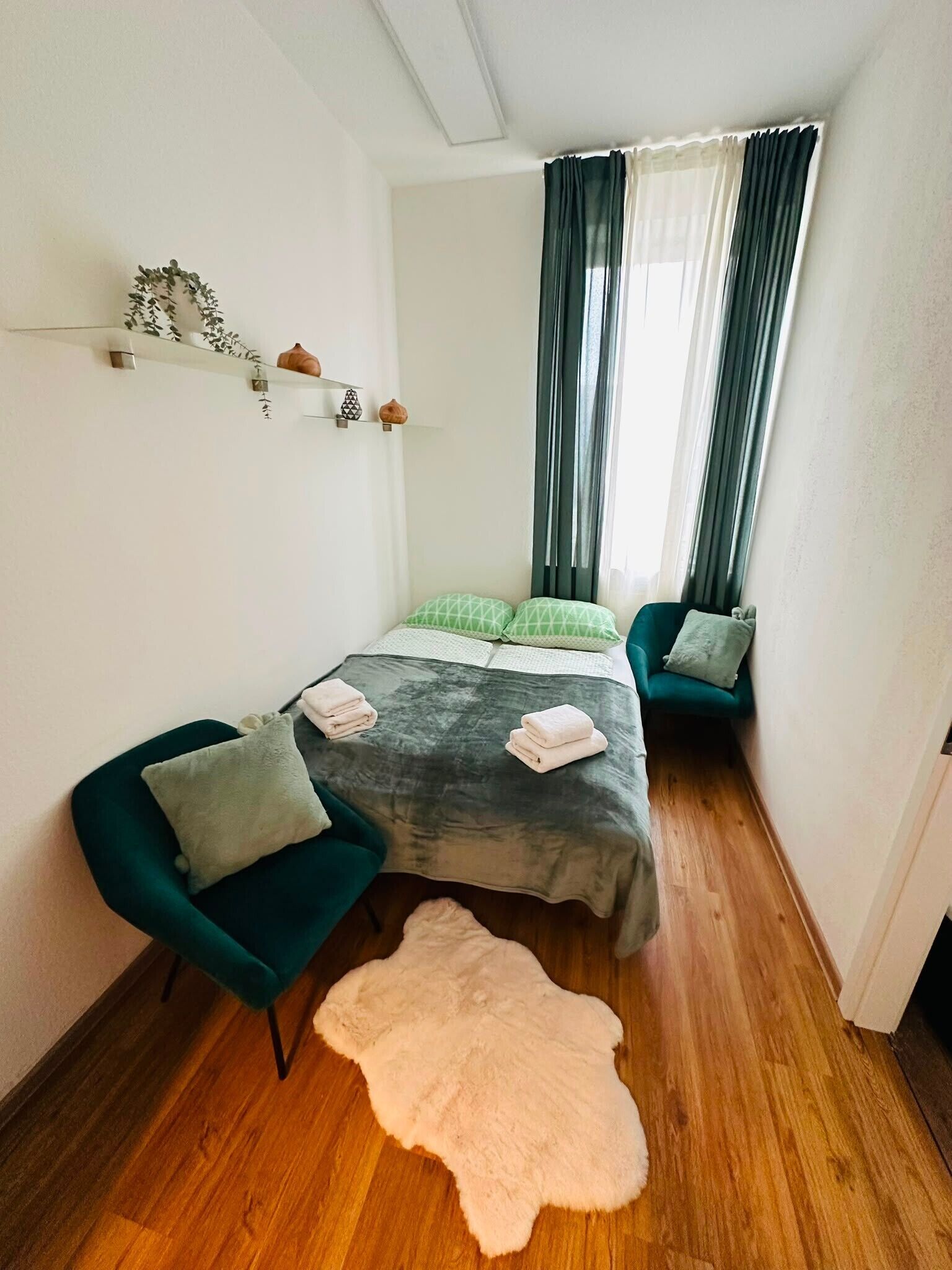 A small, cozy room with a bed, two chairs, a fur rug, and a shelf with decorative items.
