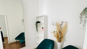 Una habitación con piso de madera, sillas color turquesa, un estante blanco y un espejo.