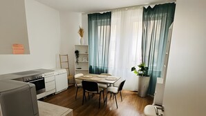 Cocina compacta con electrodomésticos modernos, comedor con mesa y sillas, y vistas al exterior a través de cortinas traslúcidas.