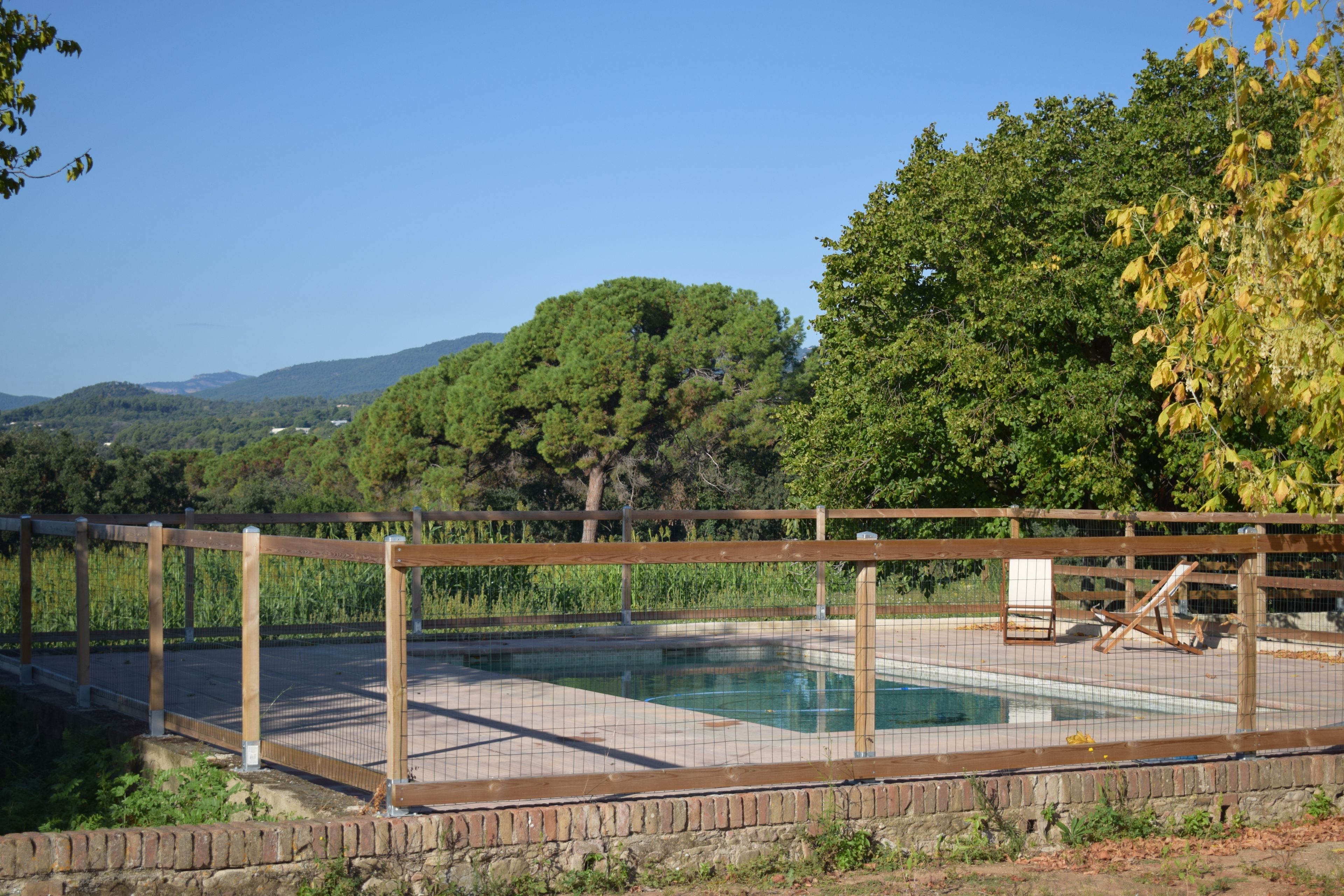 A swimming pool with a wooden fence, surrounded by trees and a clear sky.
