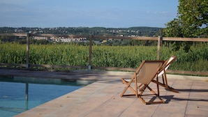 Zona de piscina con vistas a un viñedo y edificios al fondo.