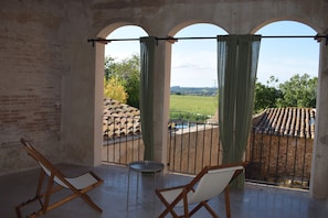 A balcony with two wooden chairs and a small table, overlooking a pool and a garden.