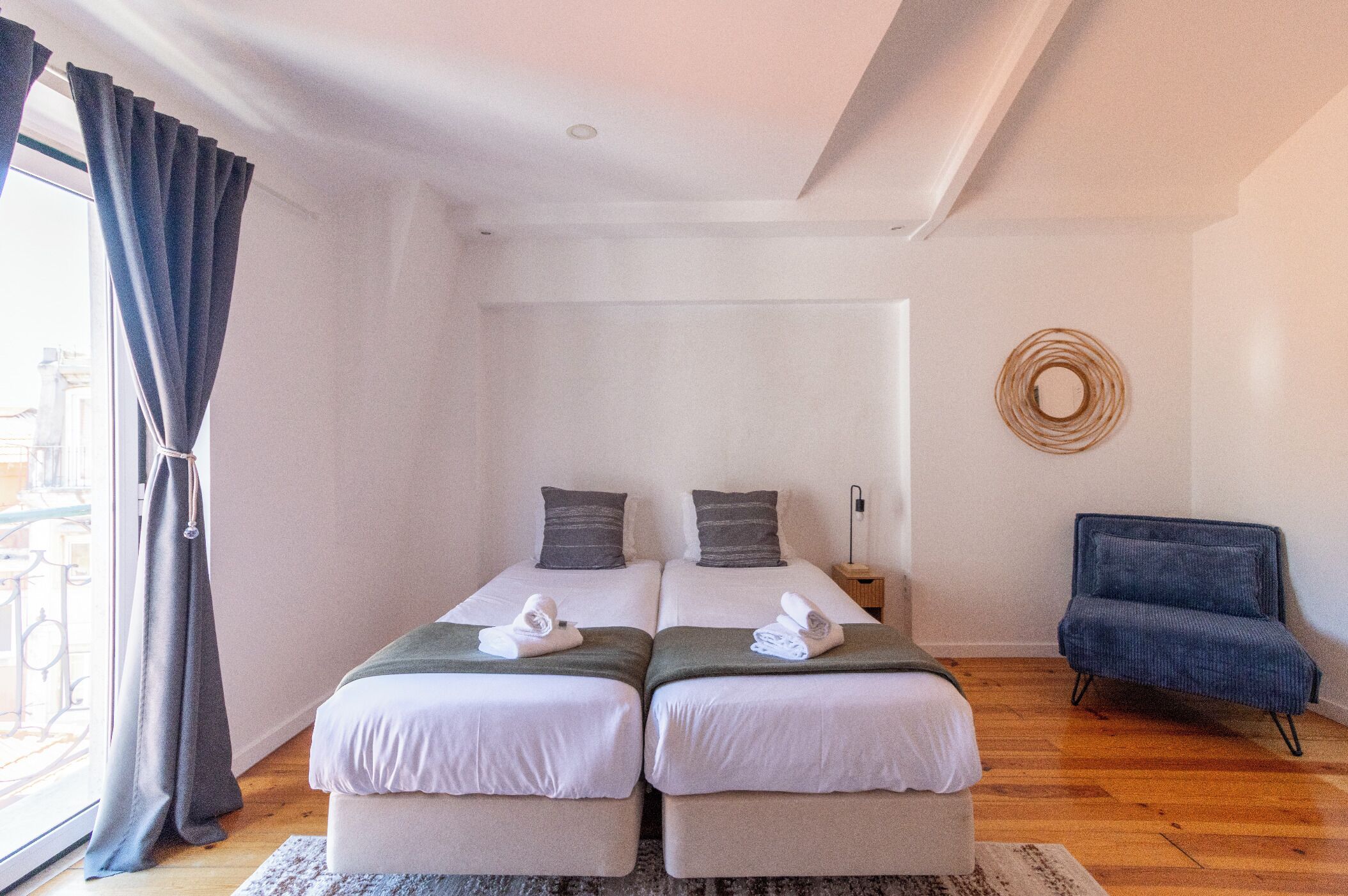 Ein Doppelzimmer mit zwei Betten, einem kleinen Beistelltisch, einem Stuhl und Blick ins Freie.