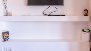 Ein an der Wand montierter Fernseher auf einem weißen Regal, ein Buch, ein Glas und eine kleine Dose.