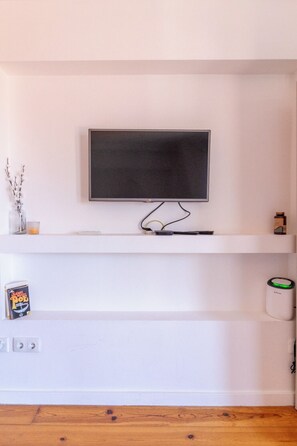 En väggmonterad tv ovanför en vit hylla, en bok, en burk och en liten behållare.