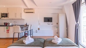 Ein kompaktes Hotelzimmer mit Küchenzeile, einem Flachbildfernseher und einem Bett mit Handtüchern.