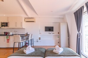 Ett kompakt hotellrum med ett litet kök, en platt-TV och en säng med handdukar.