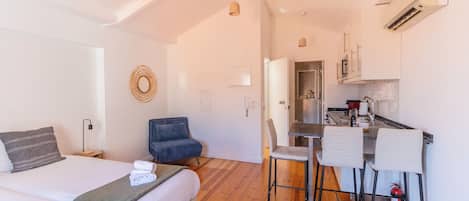 A modern hotel room with a bed, a desk, and a kitchenette.