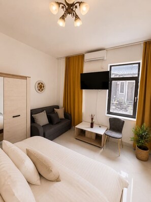 Ein Hotelzimmer mit einem Bett, einem Sofa, einem Fernseher, einem Fenster und einer Pflanze.