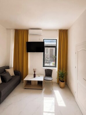 Ein stilvolles Wohnzimmer mit einer Couch, einem Couchtisch, einem Sessel, einem Fernseher und einem Fenster mit Vorhängen.