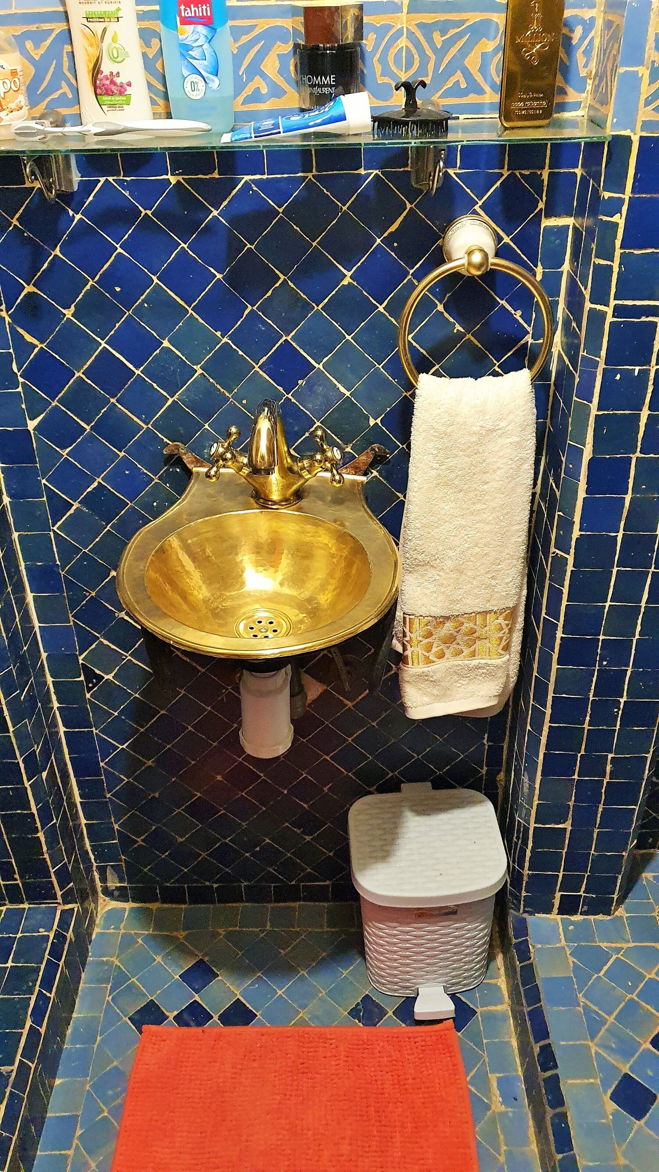 Ein Badezimmer mit einem goldfarbenen Waschbecken, einem weißen Handtuch und einem Mülleimer.