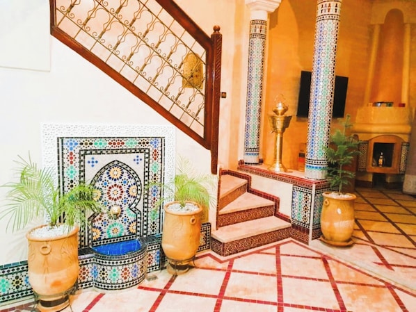 Un interior tradicional con suelo de baldosas, una escalera y un muro decorativo.