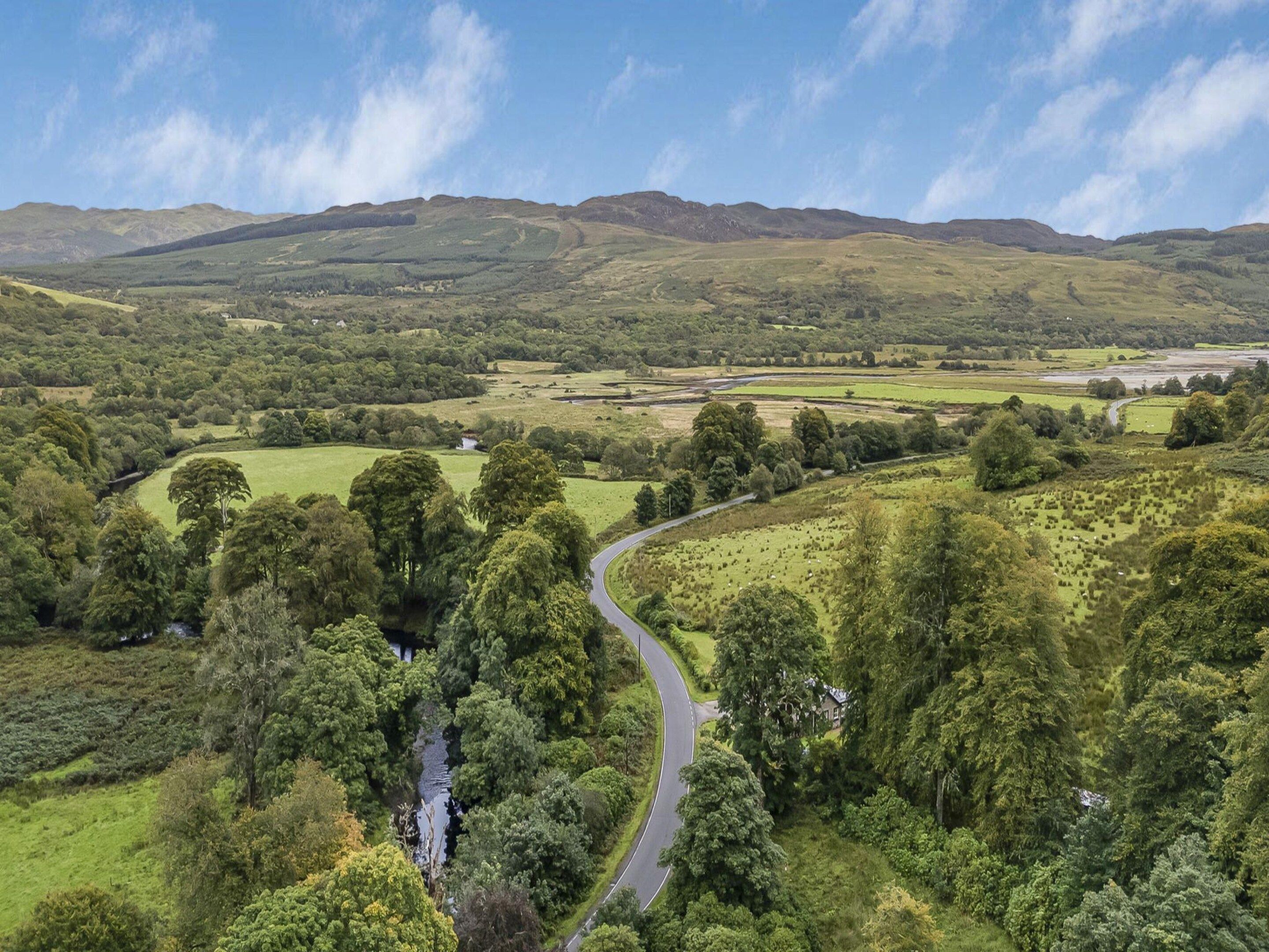 A winding road through a lush valley with hills in the background.