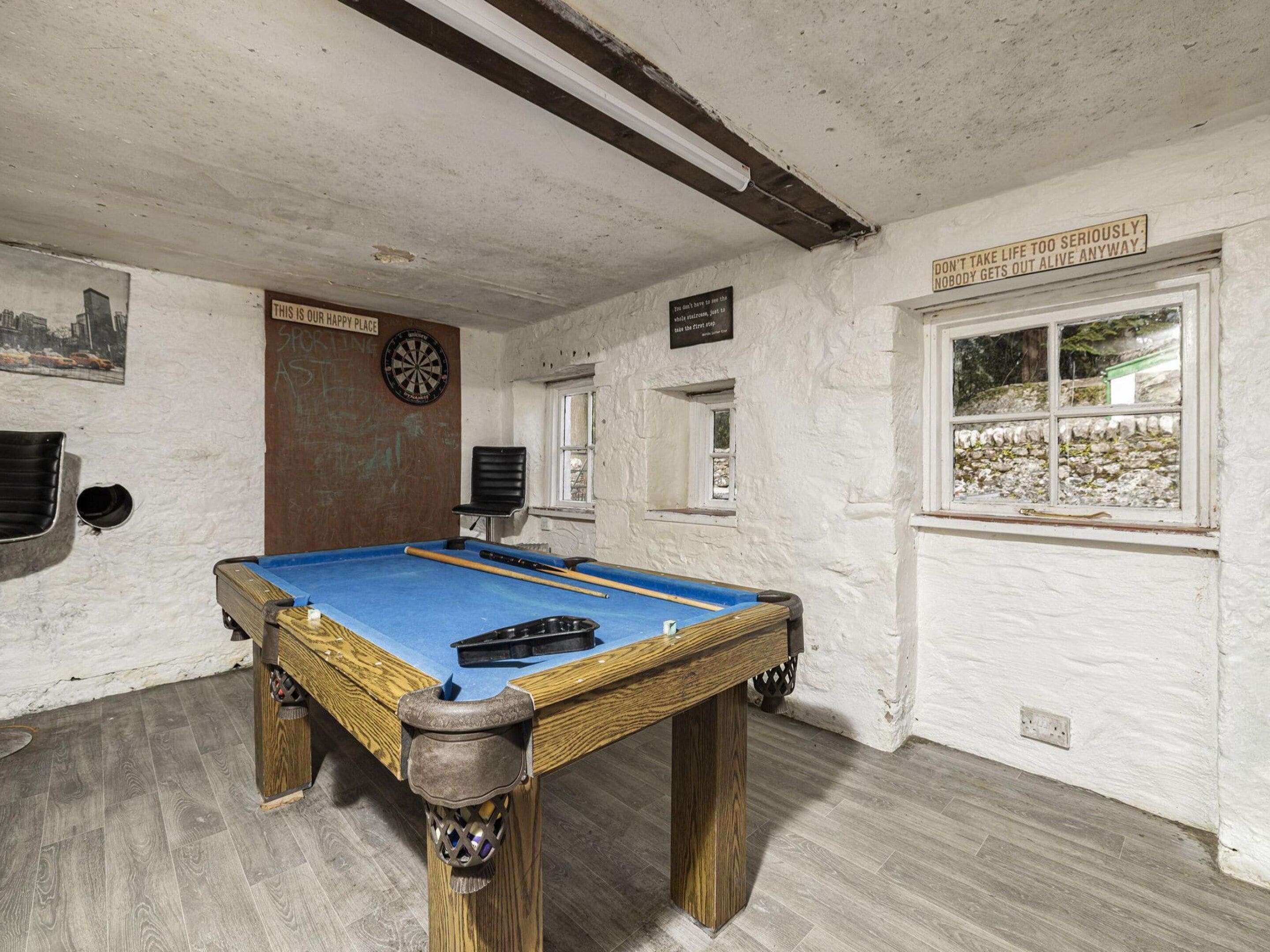 A room with a pool table, dartboard, and a window with a view.