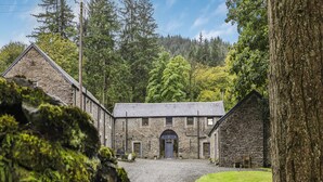 A stone building with a central entrance, surrounded by a gravel driveway and a grassy area. - 9-bedroom Scottish Retreat (Colintraive)