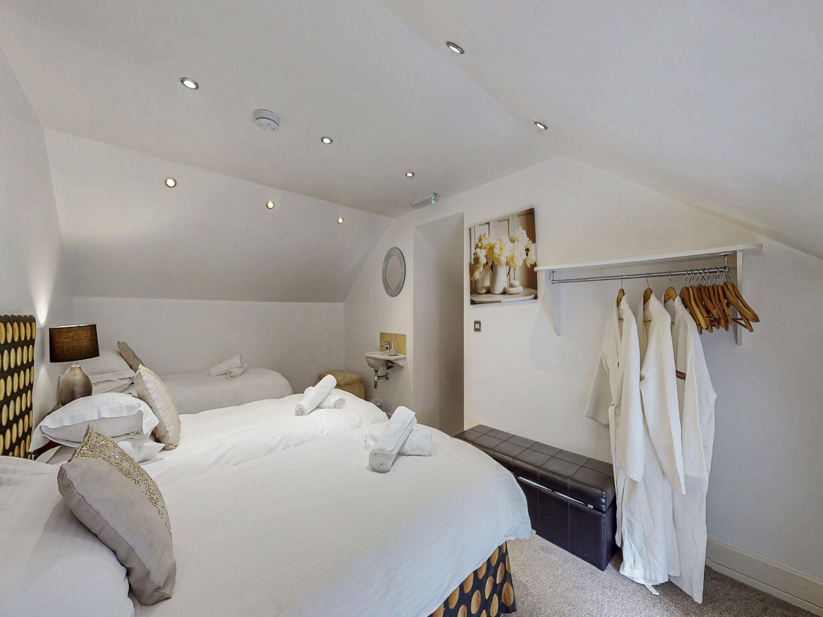 A hotel room with two beds, a bedside table, a mirror, a wall-mounted shelf with flowers, and a clothing rack.