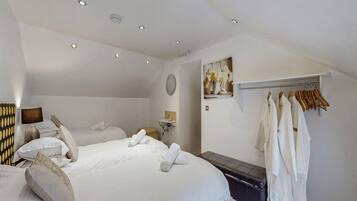 A hotel room with two beds, a bedside table, a mirror, a wall-mounted shelf with flowers, and a clothing rack.