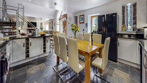 A modern kitchen with a dining area, equipped with a refrigerator, stove, and a staircase leading to an upper level. - 9-bedroom Scottish Retreat (Colintraive)