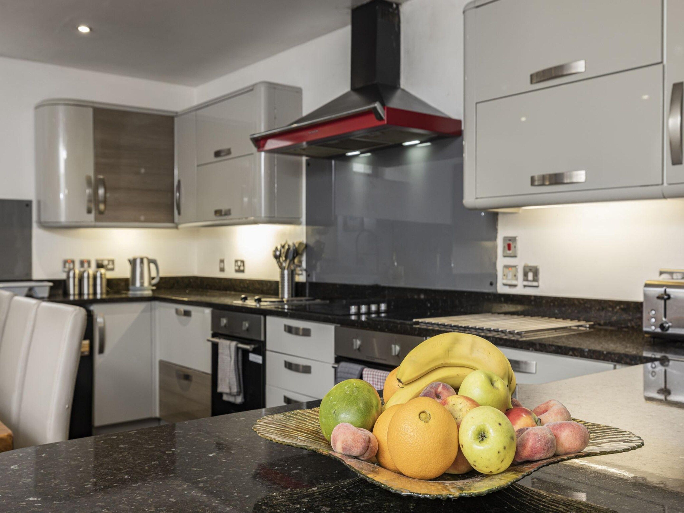 A modern kitchen with stainless steel appliances, a central island with a fruit bowl, and a range hood above the stove.