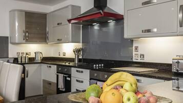 A modern kitchen with stainless steel appliances, a central island with a fruit bowl, and a range hood above the stove.