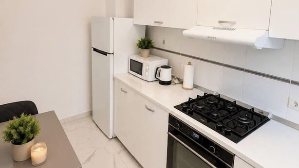 A compact kitchen with white cabinetry, a stove, oven, microwave, and a small dining table with a plant. - Cozy Bedroom Studio with Modern Kitchen & Bath (București)