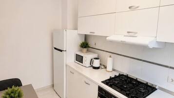 Une cuisine compacte avec des meubles blancs, une cuisinière, un four, un four à micro-ondes et une petite table à manger agrémentée d’une plante.