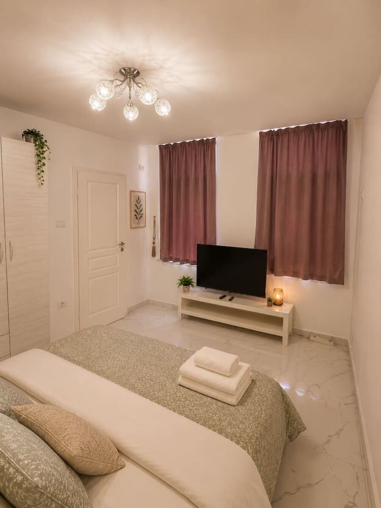 Une chambre à coucher avec un lit, un téléviseur posé sur un meuble, une table de chevet avec une lampe et une fenêtre avec des rideaux.