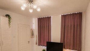 A bedroom with a bed, a TV on a stand, a bedside table with a lamp, and a window with curtains. - Cozy Bedroom Studio with Modern Kitchen & Bath (București)