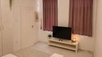 Une chambre à coucher avec un lit, un téléviseur posé sur un meuble, une table de chevet avec une lampe et une fenêtre avec des rideaux.