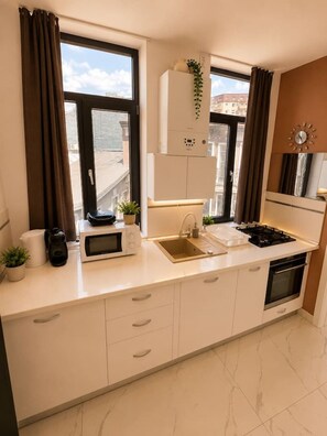 Eine moderne Küche mit integriertem Mikrowellenherd, Herd und Spüle. Über der Arbeitsplatte befinden sich Schränke und ein Fenster mit Vorhängen.