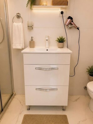 Ein Badezimmer mit weißem Waschtisch, Handtuchhalter, Fön, Pflanze und Toilette.