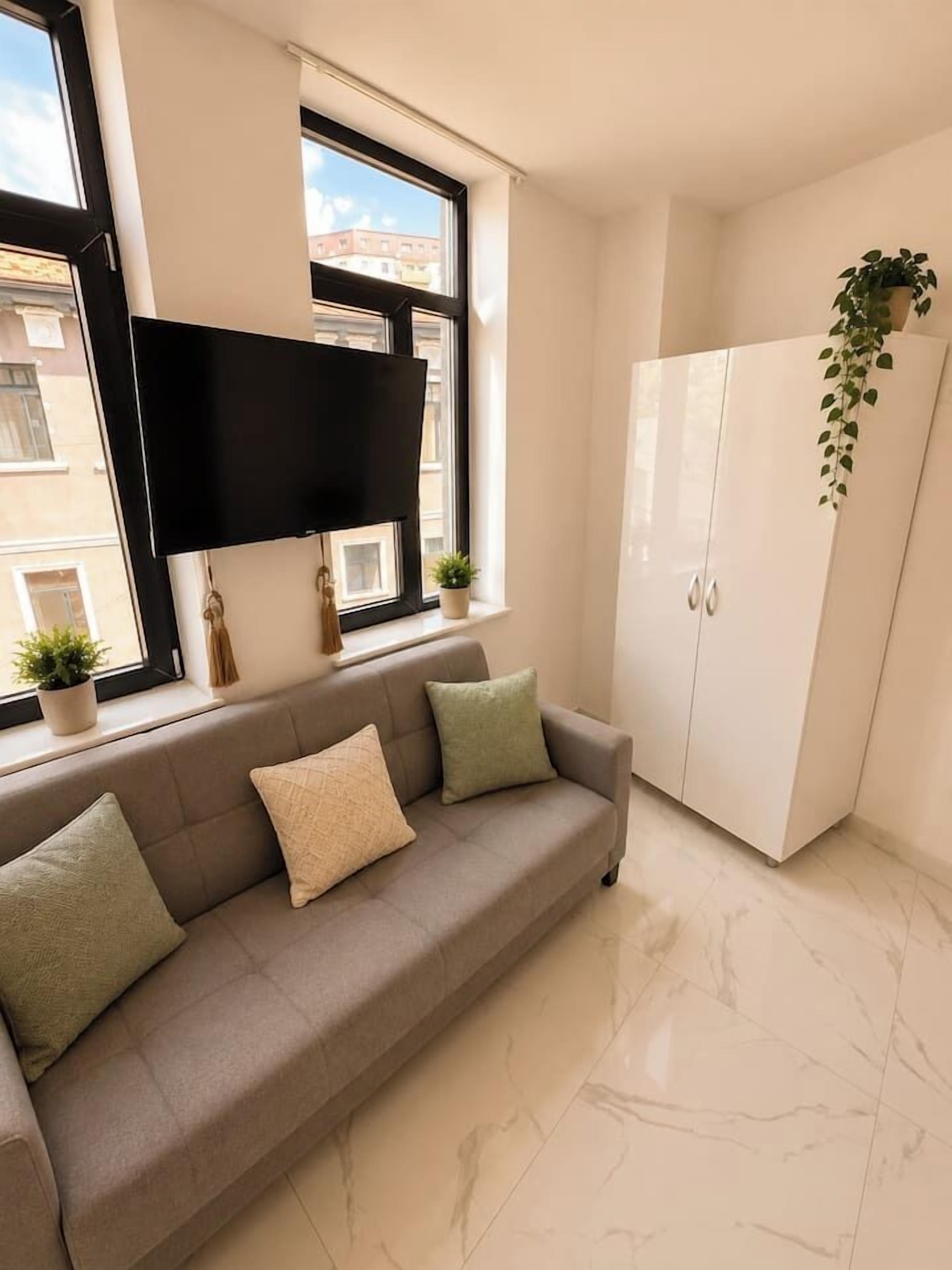A modern living room with a sofa, a flat-screen TV mounted on the wall, a cabinet, and a hanging plant.
