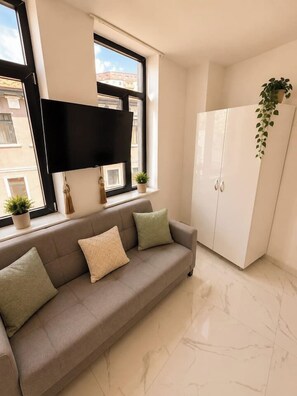 A modern living room with a sofa, a flat-screen TV mounted on the wall, a cabinet, and a hanging plant. - Stylish 1-Bedroom Apartment with Warm Accents (București)