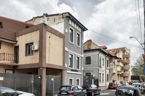 Vista da rua com edifícios residenciais de vários andares, carros estacionados e céu claro.