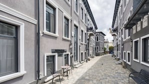 A narrow street with uniform gray buildings, a paved walkway, and outdoor seating. - Charming Studio in a Historic Bucharest Courtyard (București)