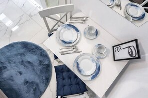 Uma sala de jantar com uma mesa branca posta para quatro pessoas, incluindo pratos, talheres e uma chávena.