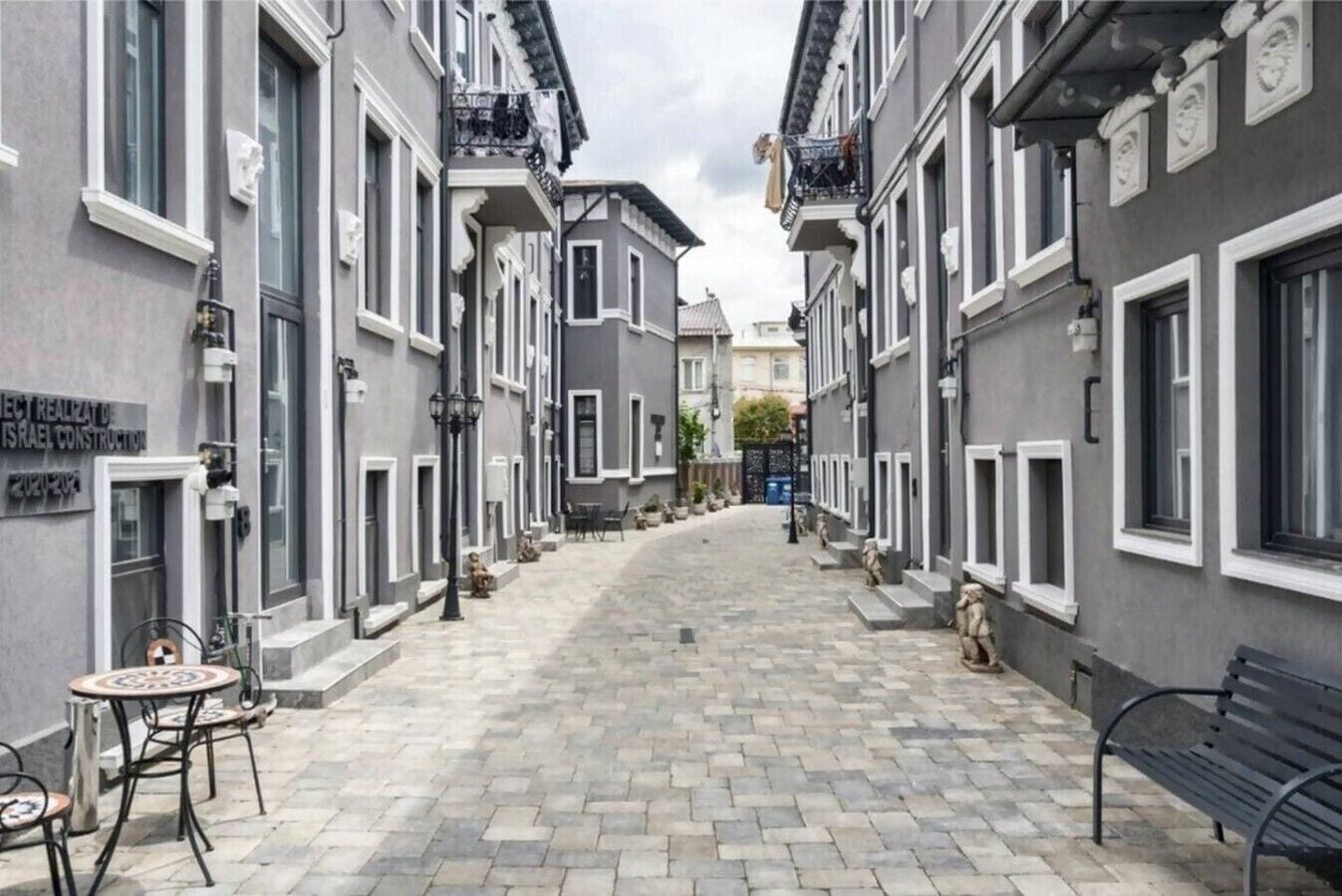 A narrow street lined with buildings, a bench, and a table with chairs.