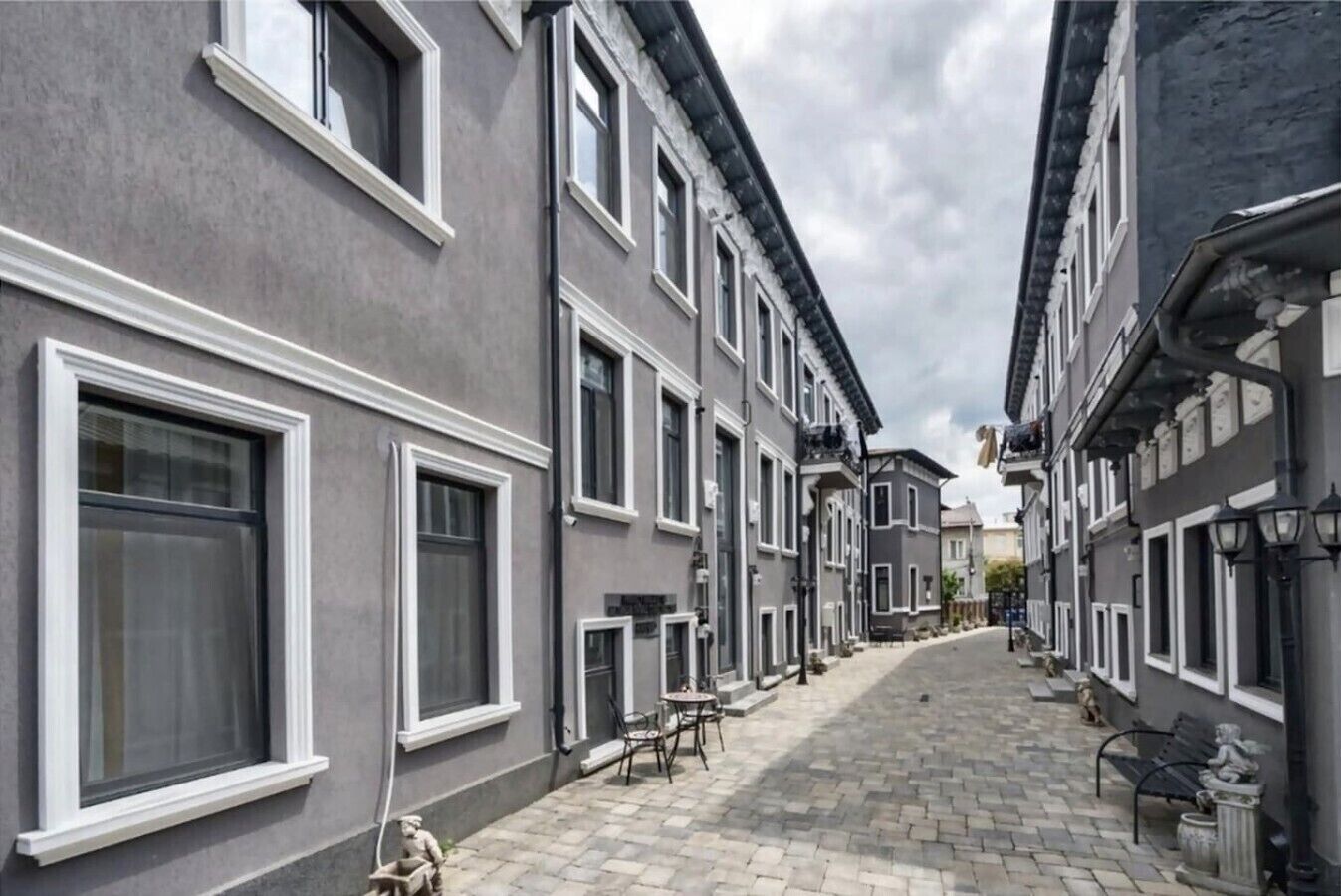 Uma rua estreita com edifícios cinzentos e uniformes, molduras de janelas brancas e um passeio pavimentado.