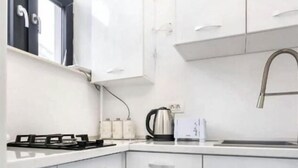 A compact kitchen with white cabinets, a gas stove, a kettle, and a sink. - Charming Studio in a Historic Bucharest Courtyard (București)