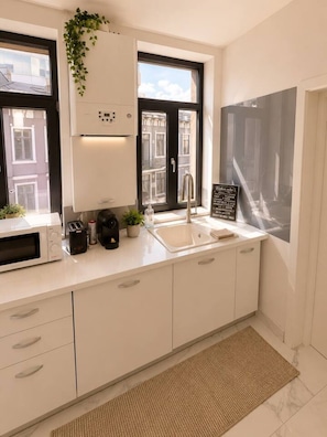 Een moderne keuken met witte kastjes, een magnetron, een broodrooster, een spoelbak en een raam met uitzicht op gebouwen.