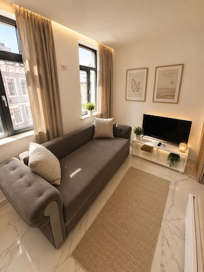 Een moderne woonkamer met een bank, een flatscreen televisie en een raam met gordijnen.