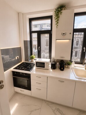 Eine moderne Küche mit Gasherd, Mikrowelle und Backofen, weißen Schränken, einem Spülbecken und einem Fenster mit Blick auf Gebäude.