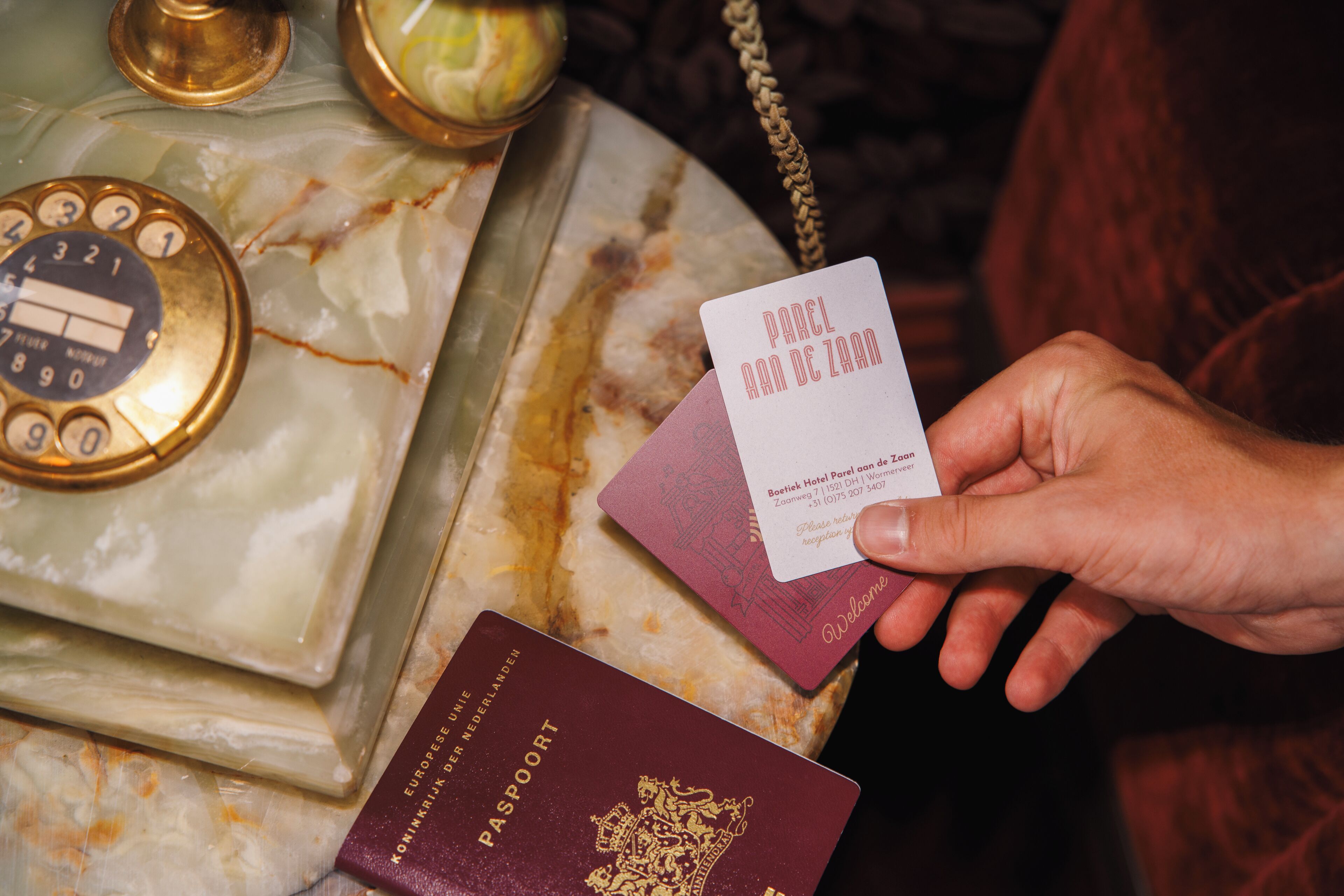 A hand holding a business card and a passport, with a marble table and a golden object in the background.