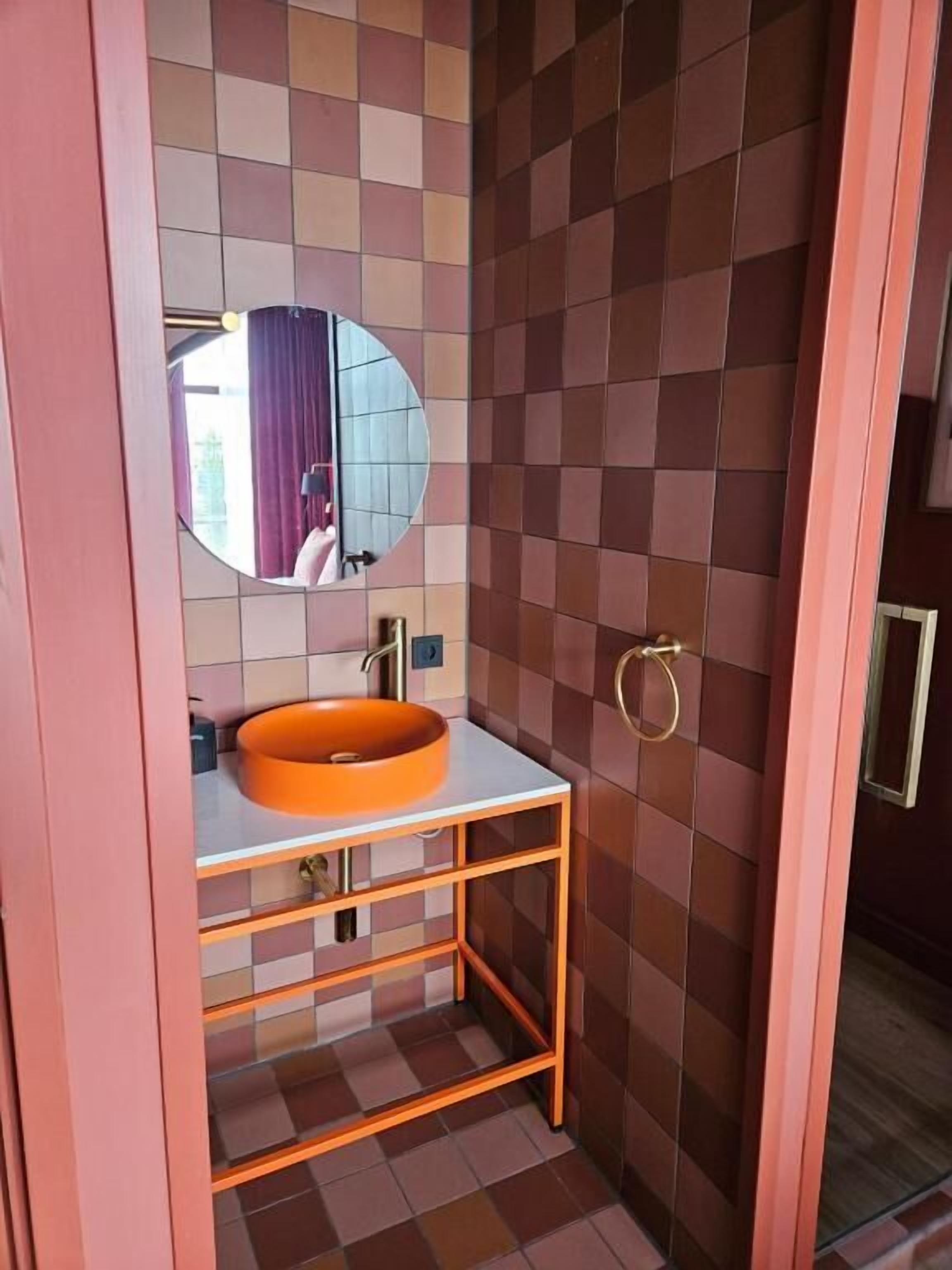 A bathroom with a round orange sink, a mirror, and a tiled wall.