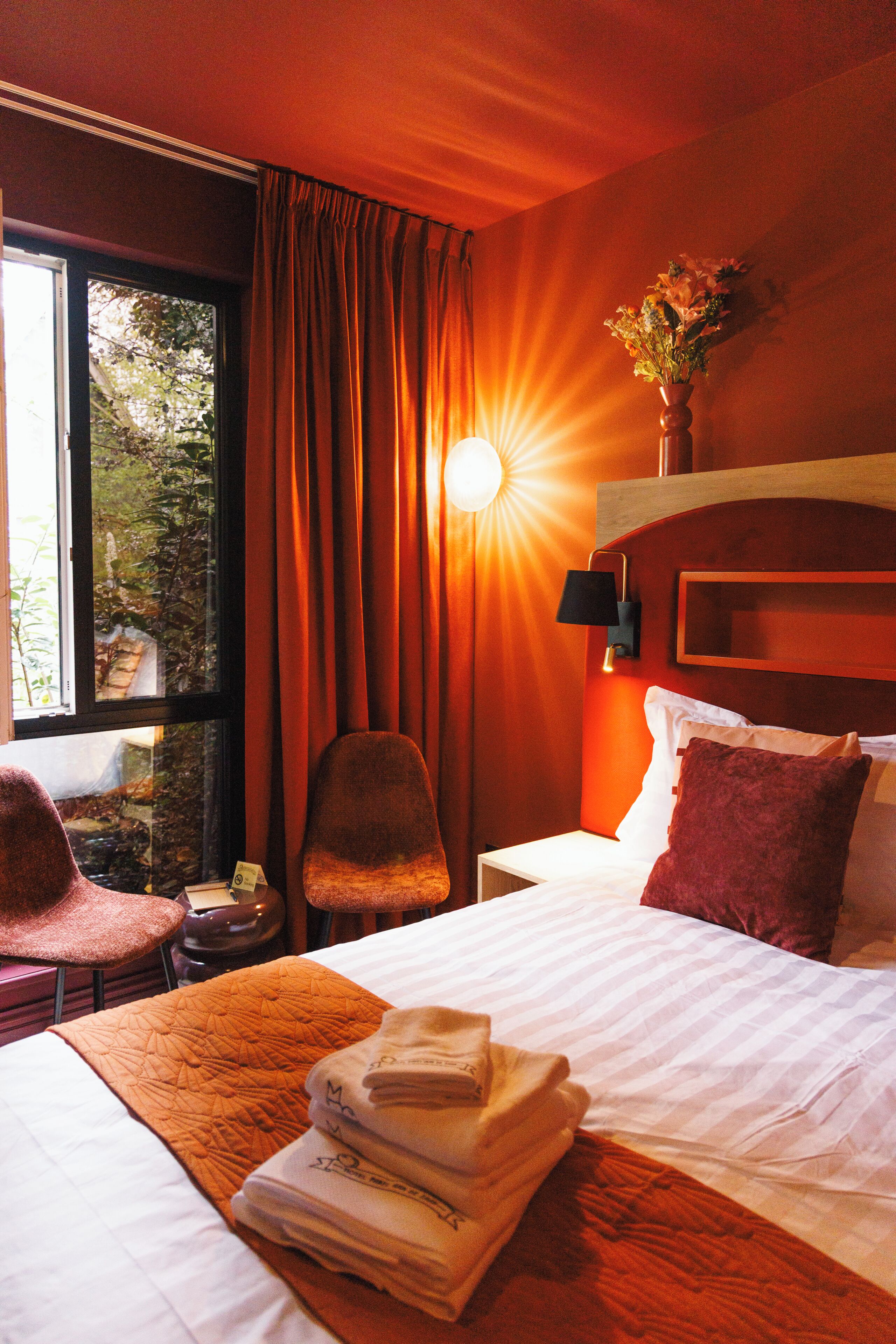 Ein Hotelzimmer mit Bett, Stuhl, Nachttisch und einem Fenster mit Vorhängen.